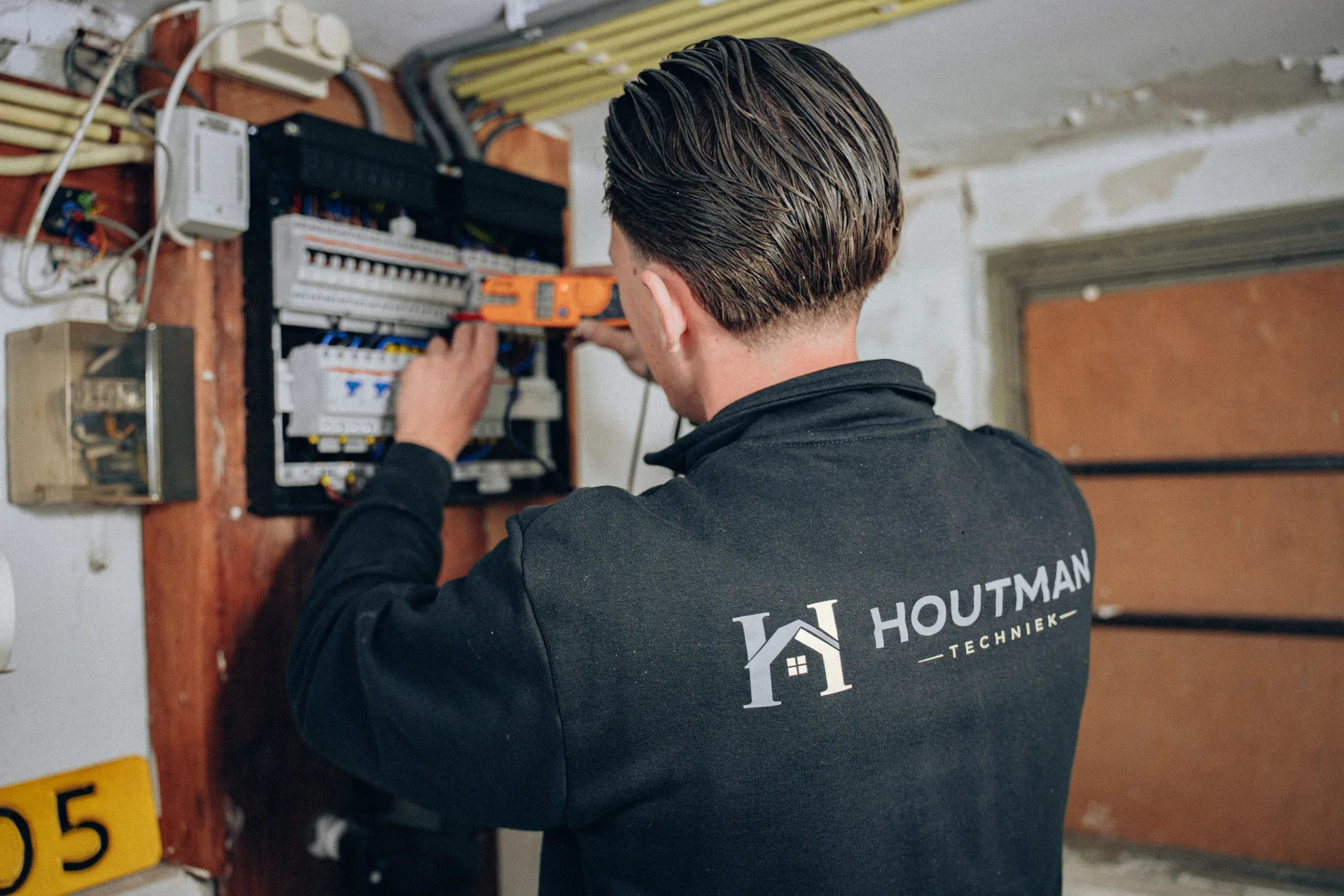 Monteur met Houtman Techniek-logo op rug werkt aan groepenkast