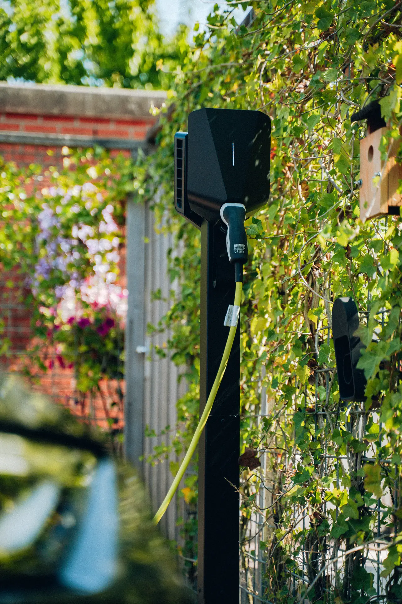 Laadpaal met aangesloten laadkabel naast een tuinmuur